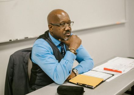 Mature teacher sitting at desk proctoring an examination in a classroom.