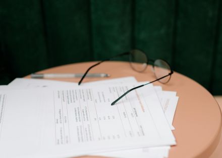 A close-up of documents, eyeglasses, and a pen on a round table indoors.