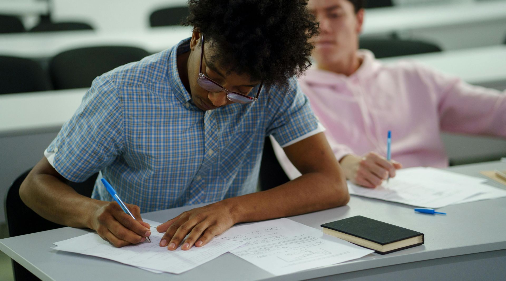 Two students focused on studying and writing notes in a classroom.